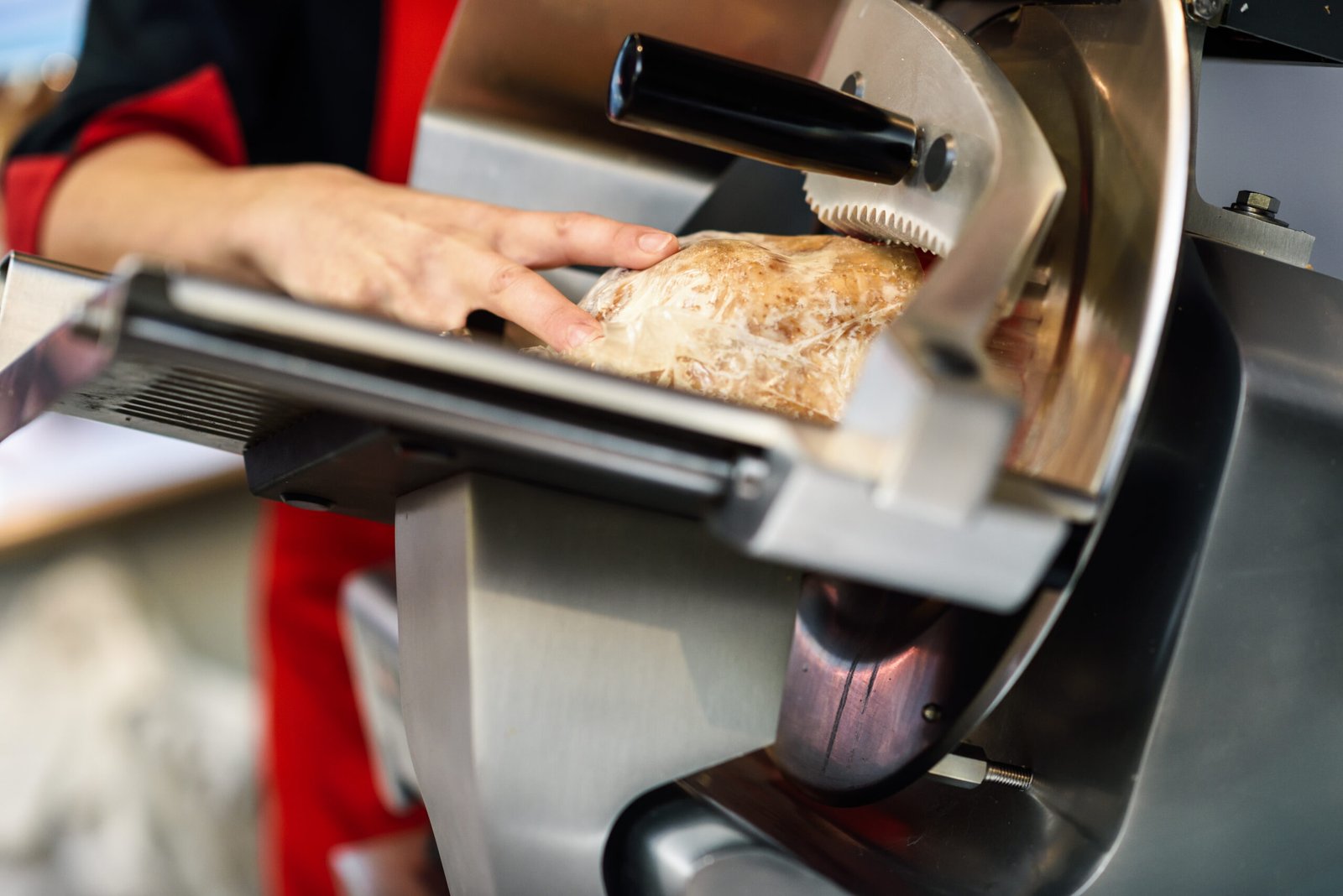 Close-up of female butcher cutting york ham in a cutting machine inside a butcher shop.